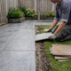 Moderne Nederlandse achtertuin met grote 60x60 tuintegels op een strak terras, waar een huiseigenaar materiaal en dikte vergelijkt in zacht daglicht.
