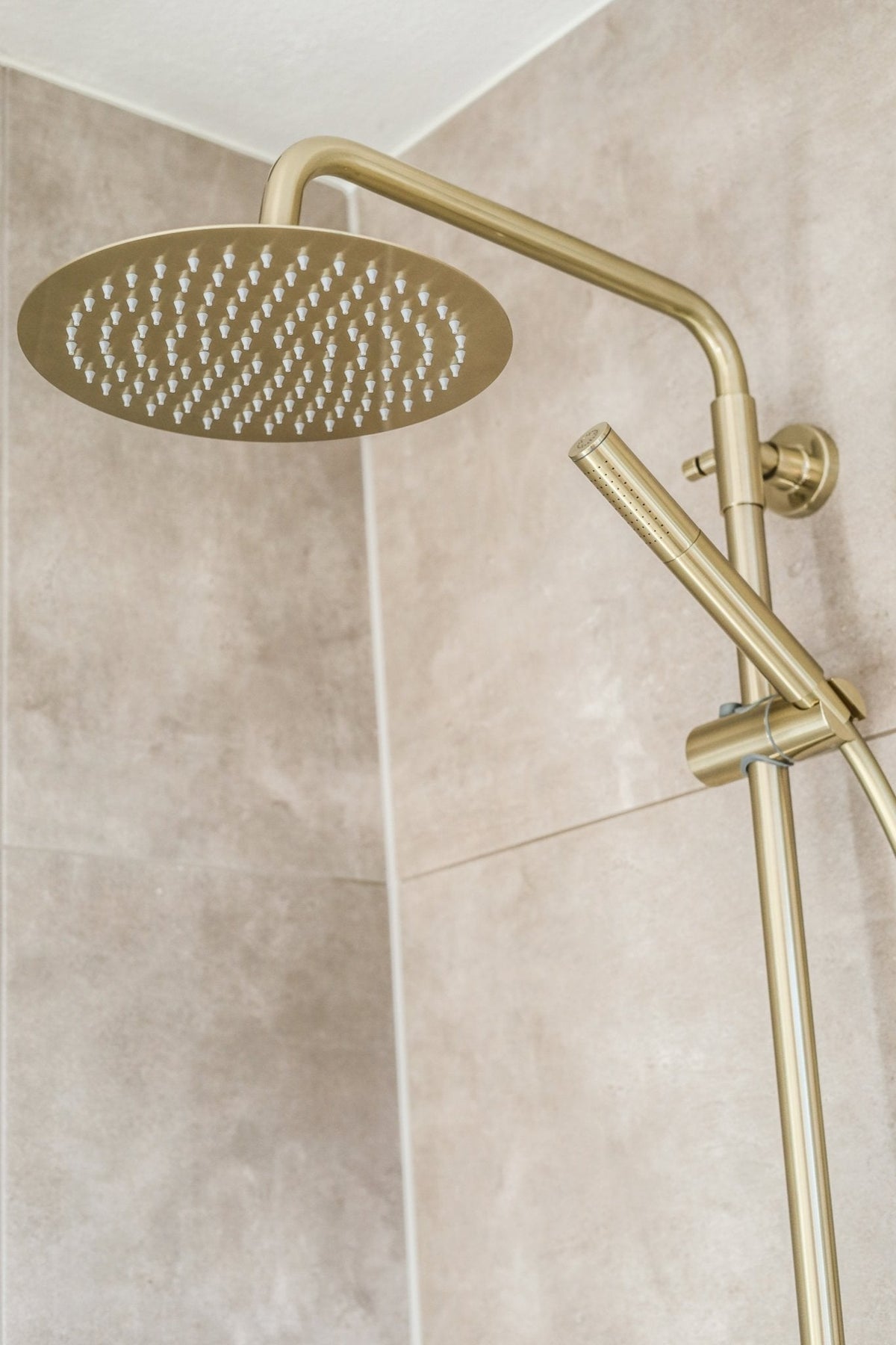 Gouden hoofddouche en handdouche Novi aan een betegelde wand
